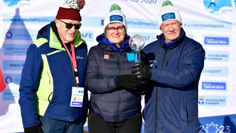 A man standing next to a woman and another man holding a trophy