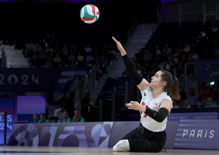 A female sitting volleyball player is serving the ball during competition
