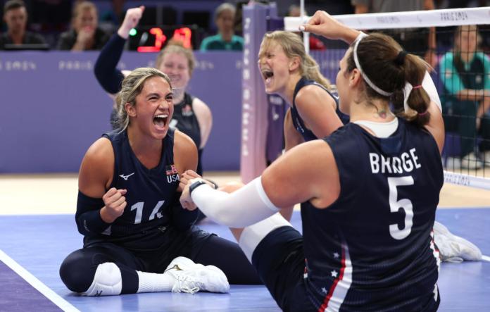 A female sitting volleyball player pumps her fist during a game to celebrate with her teammates